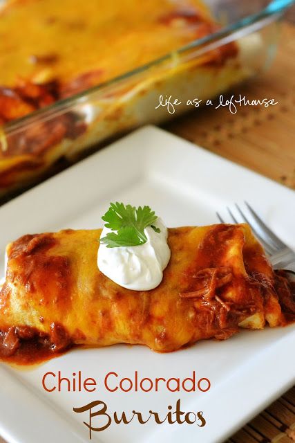 an enchilada on a white plate with sour cream and cilantro