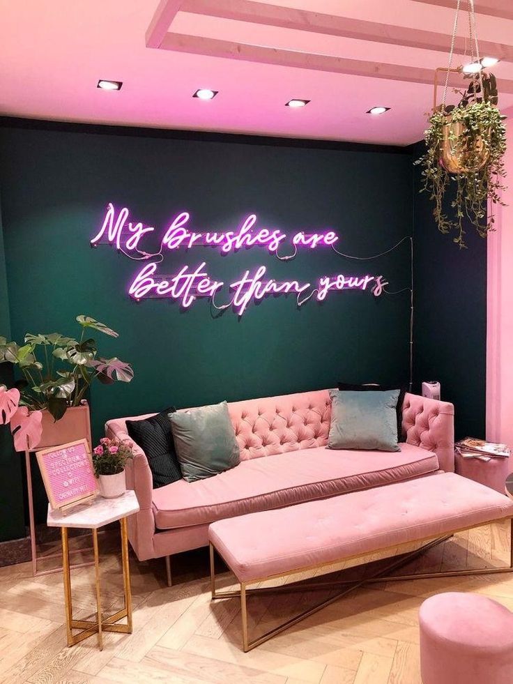 a pink couch sitting next to a green wall with neon writing on the wall above it