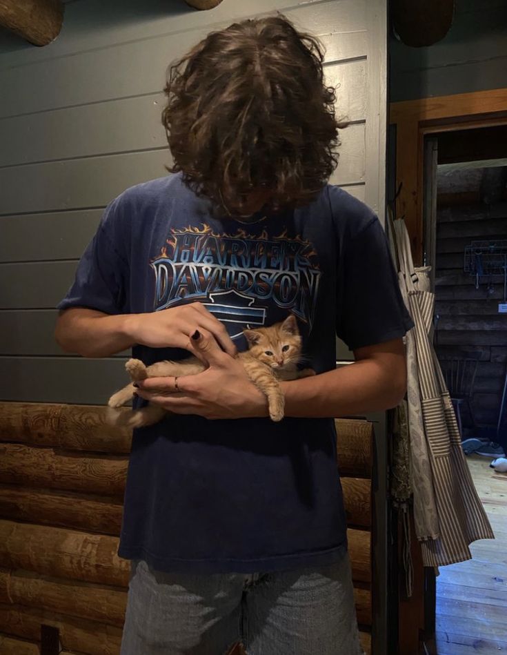 a man holding a cat in his hands while standing next to a wooden wall and door