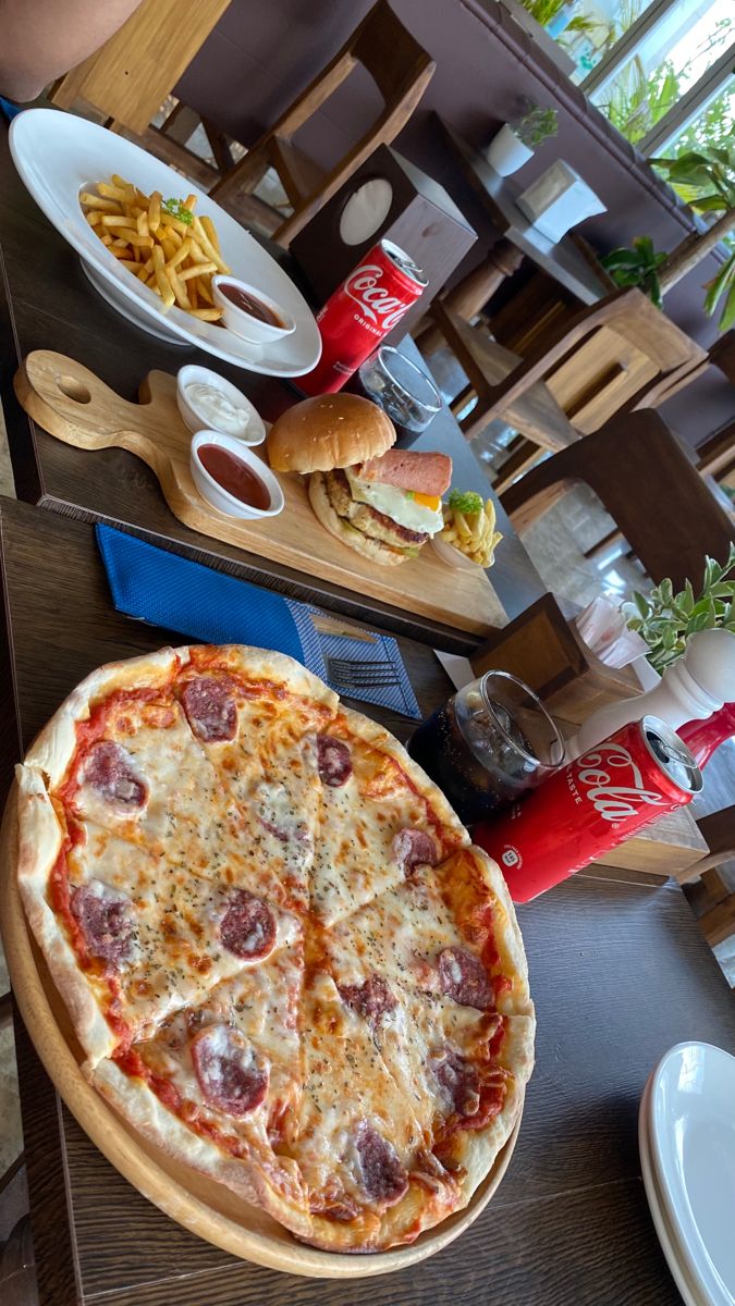 a pizza sitting on top of a wooden table next to a plate of fries and ketchup