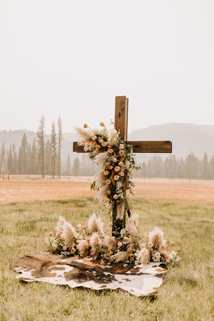 a cross sitting on top of a lush green field next to a wooden pole with flowers