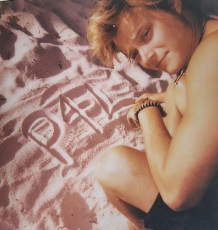 a woman sitting in the sand with her hand on her chest and writing on it