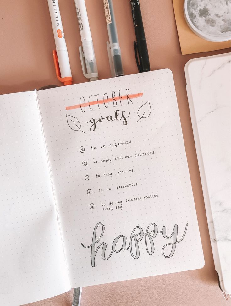 an open notebook with the words happy written in cursive writing on it, surrounded by office supplies