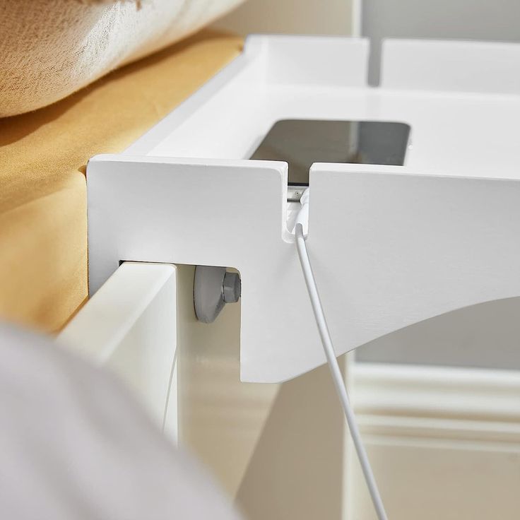 an iphone is plugged in to the side of a white desk with two drawers