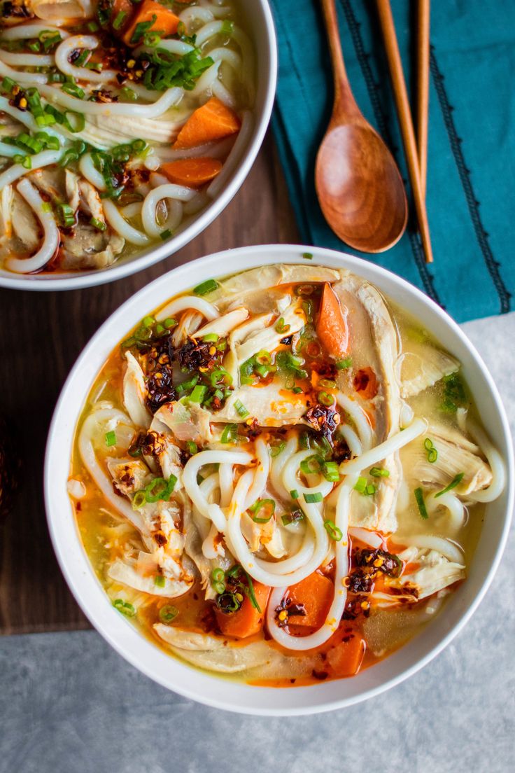 two bowls filled with noodles and vegetables next to chopsticks