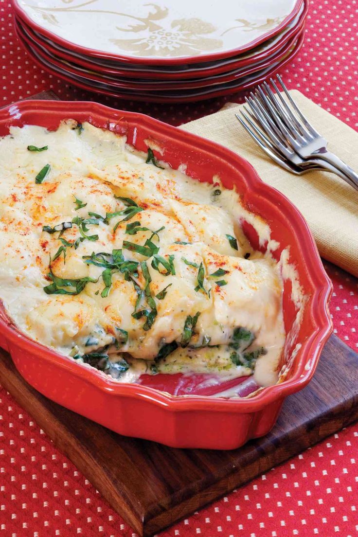 a red casserole dish filled with mashed potatoes and spinach garnished with cheese