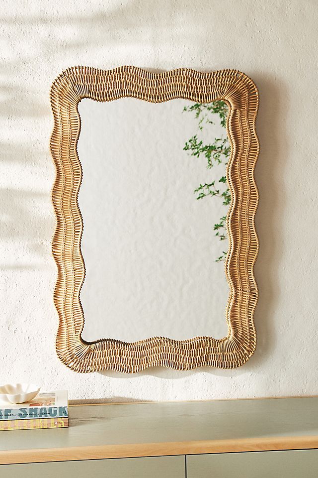 a mirror sitting on top of a wooden dresser next to a plant in a vase