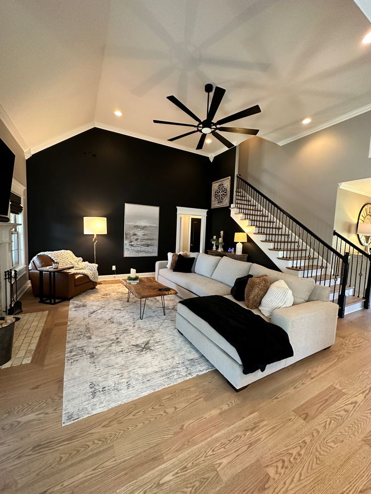 a living room with white couches and black walls, hardwood floors and a ceiling fan