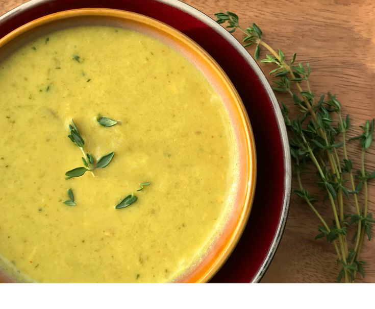 a red bowl filled with soup on top of a wooden table next to a green sprig