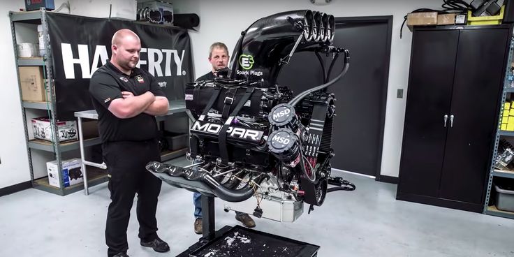 two men standing next to an engine in a garage