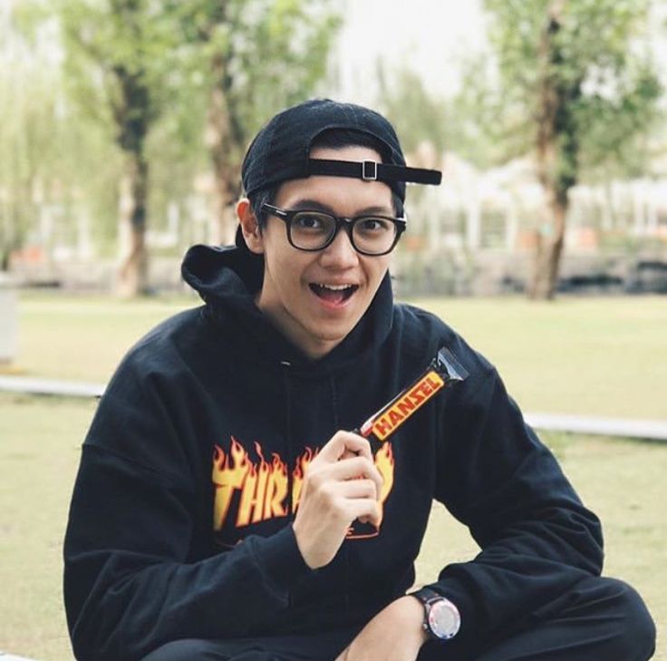 a young man sitting on the ground wearing glasses and holding a candy bar in his hand