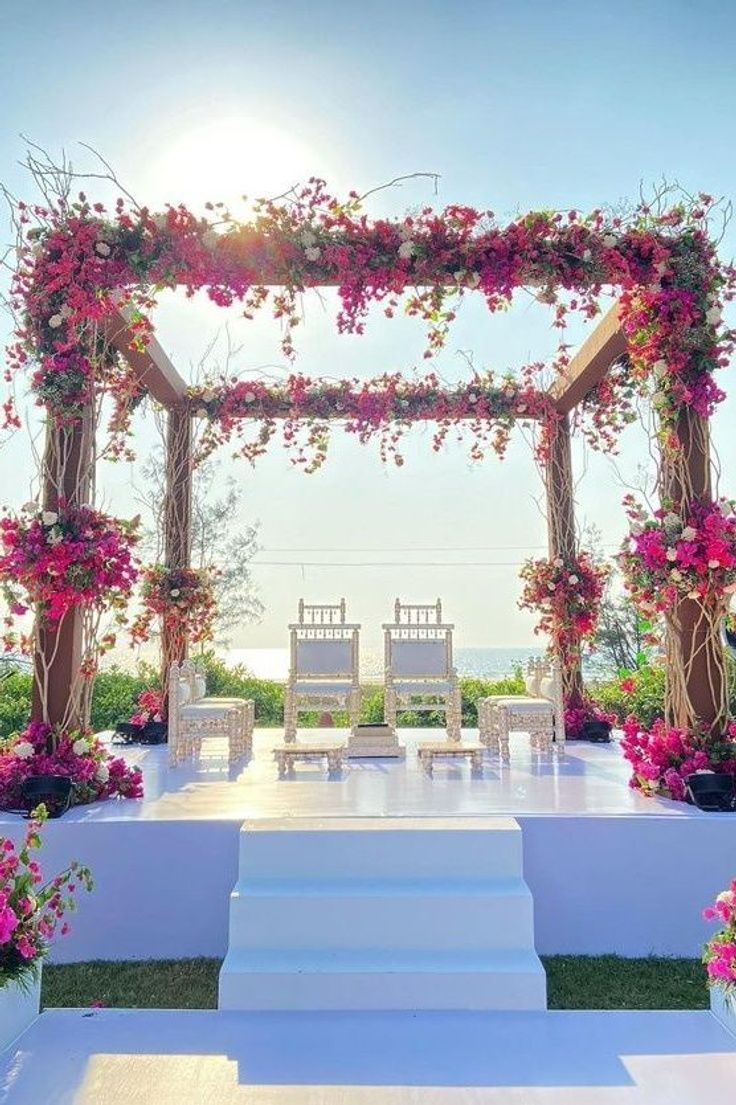 an outdoor wedding setup with white chairs and pink flowers on the steps leading up to it