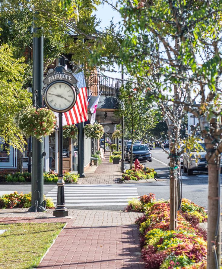 an american flag hanging on the side of a building next to a clock and flowers