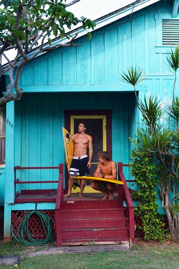 two men standing in the doorway of a blue house with surfboards on their feet