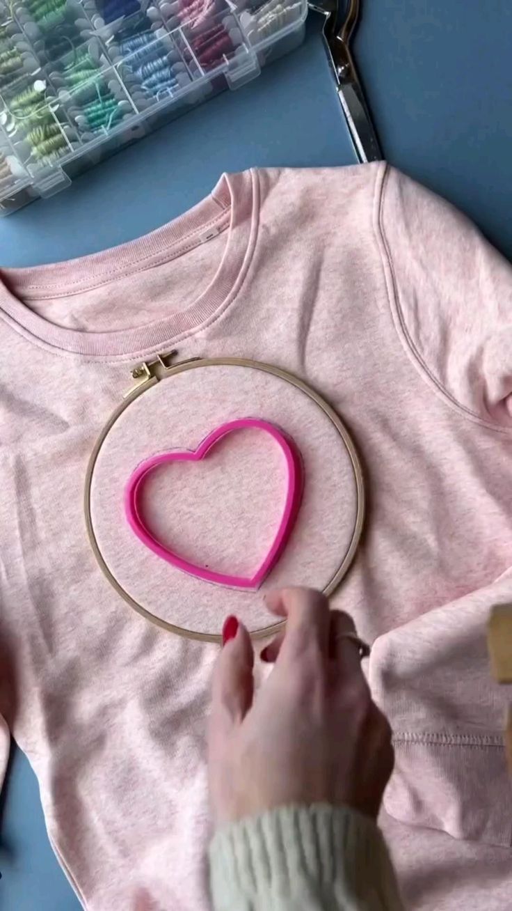 someone is making a heart shaped t - shirt with pink thread and scissors on the table