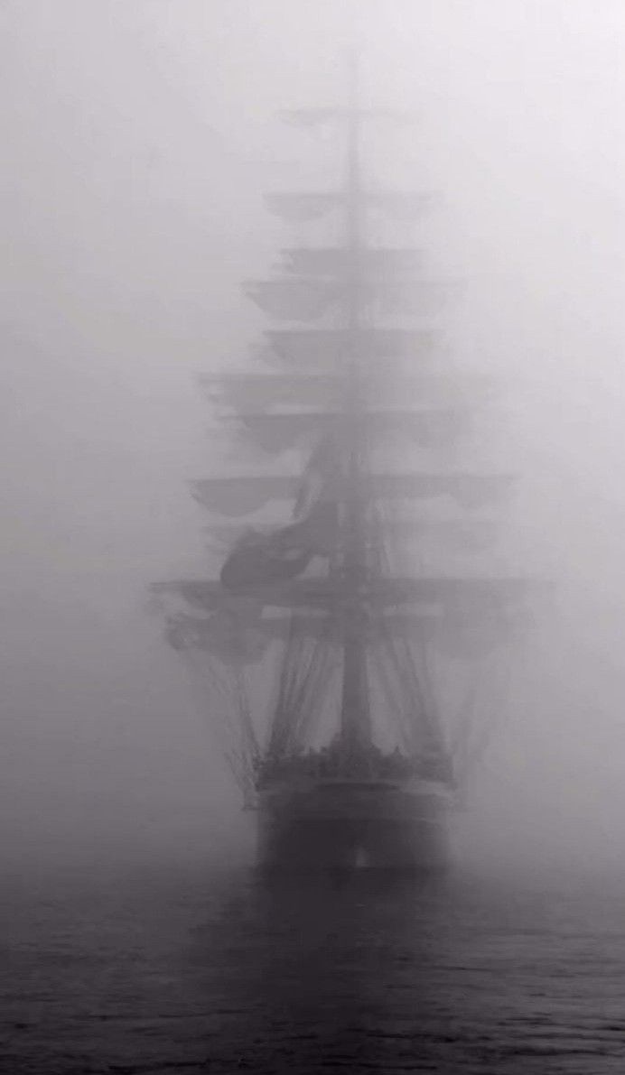 a tall ship in the middle of foggy water with it's sails down