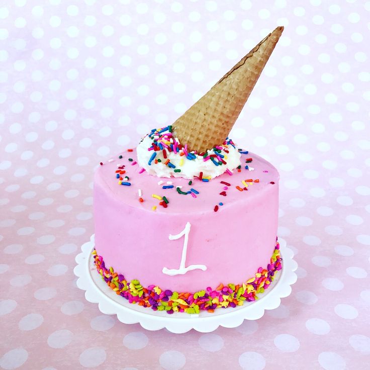 a pink birthday cake with an ice cream cone on top and sprinkles