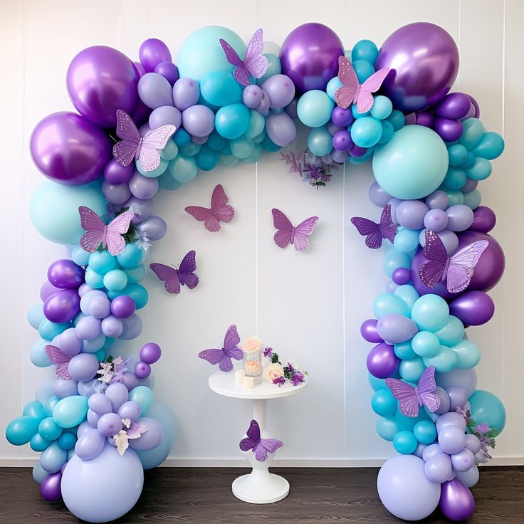 the balloon arch is decorated with purple and blue balloons, butterflies, and a cake