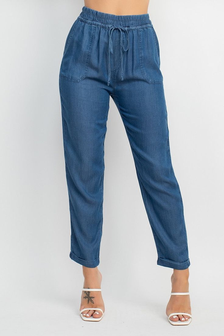 A pair of denim jogger pants featuring a high-rise elastic waistband, relaxed fit, cuffed hem, waistband, self-tie drawstring, pockets, and a full length. Fabric: 100% LYOCELL Made in Egypt Trendy Paperbag Waist Pants With Elastic Waistband, Casual Cargo Jeans For Fall, Casual Spring Joggers With Pull-on Style, Casual Straight Leg Joggers With Elastic Waistband, Relaxed Fit Paperbag Waist Bottoms With Pockets, Casual Denim Blue Tencel Jeans, Spring Cropped Leg Cargo Jeans With Relaxed Fit, Spring Cargo Jeans With Relaxed Fit And Cropped Leg, Spring Relaxed Fit Joggers With Pockets