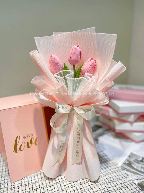 pink tulips in a vase with ribbon tied around it and two boxes on the table