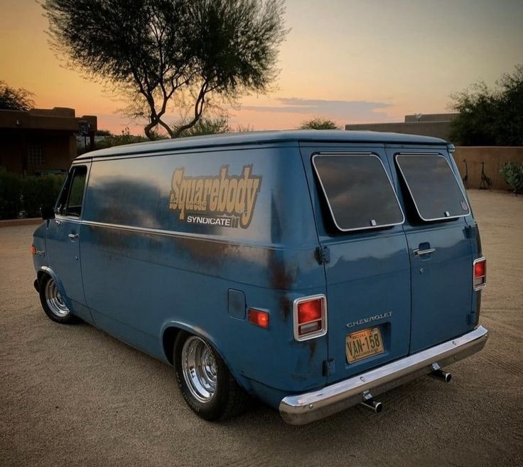 an old blue van parked in a parking lot with the sun setting on it's horizon