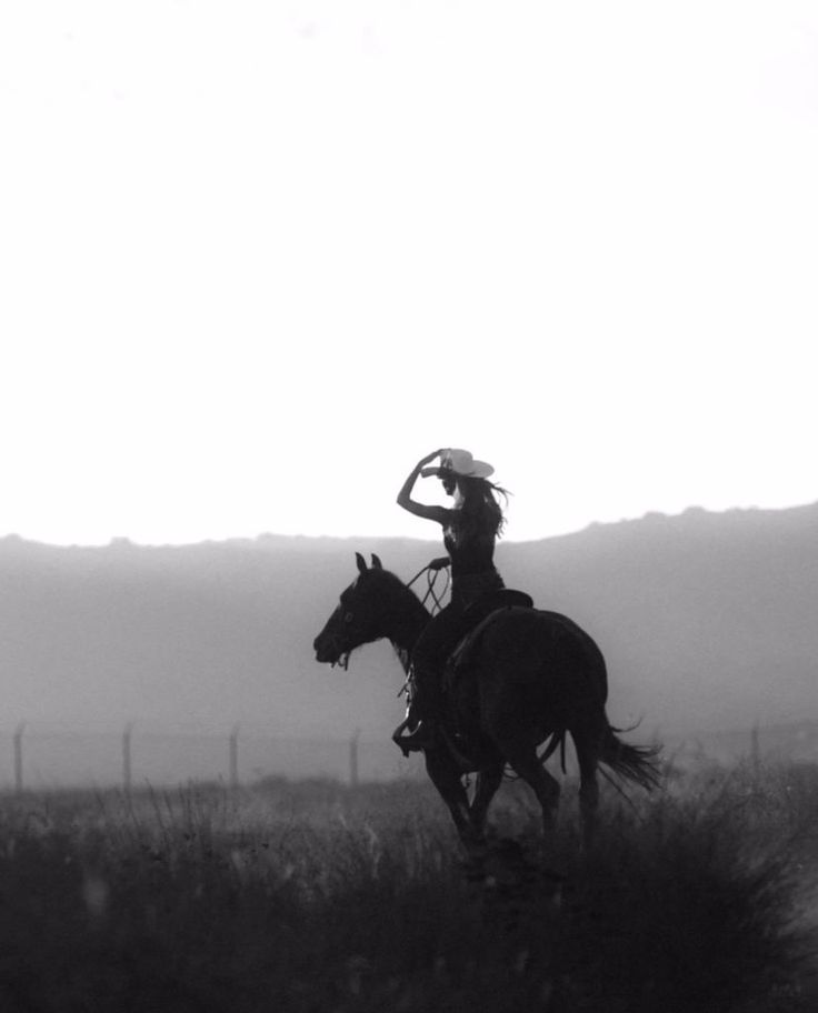 a woman riding on the back of a horse across a lush green field with mountains in the background