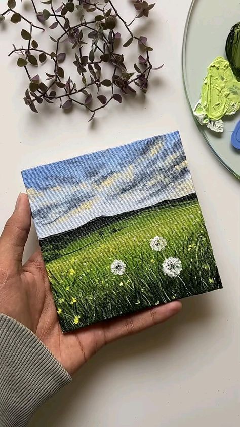 a person holding up a painting on top of a table next to flowers and plates