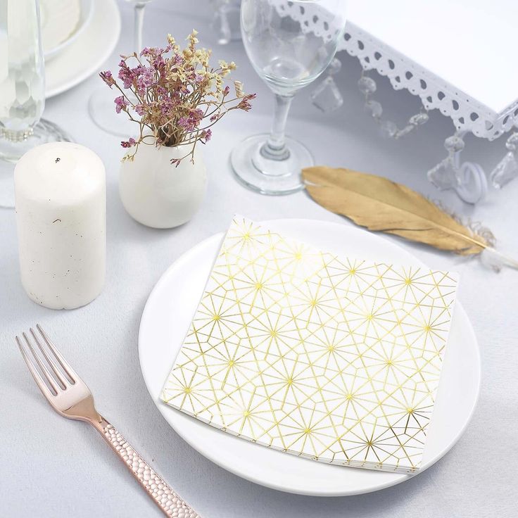 a white plate topped with a napkin next to a vase filled with flowers and candles