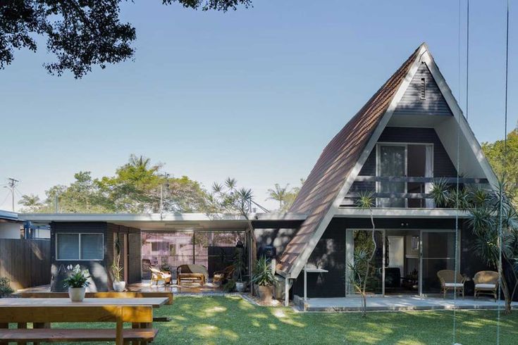 a house that is sitting in the grass with a picnic table and chairs around it