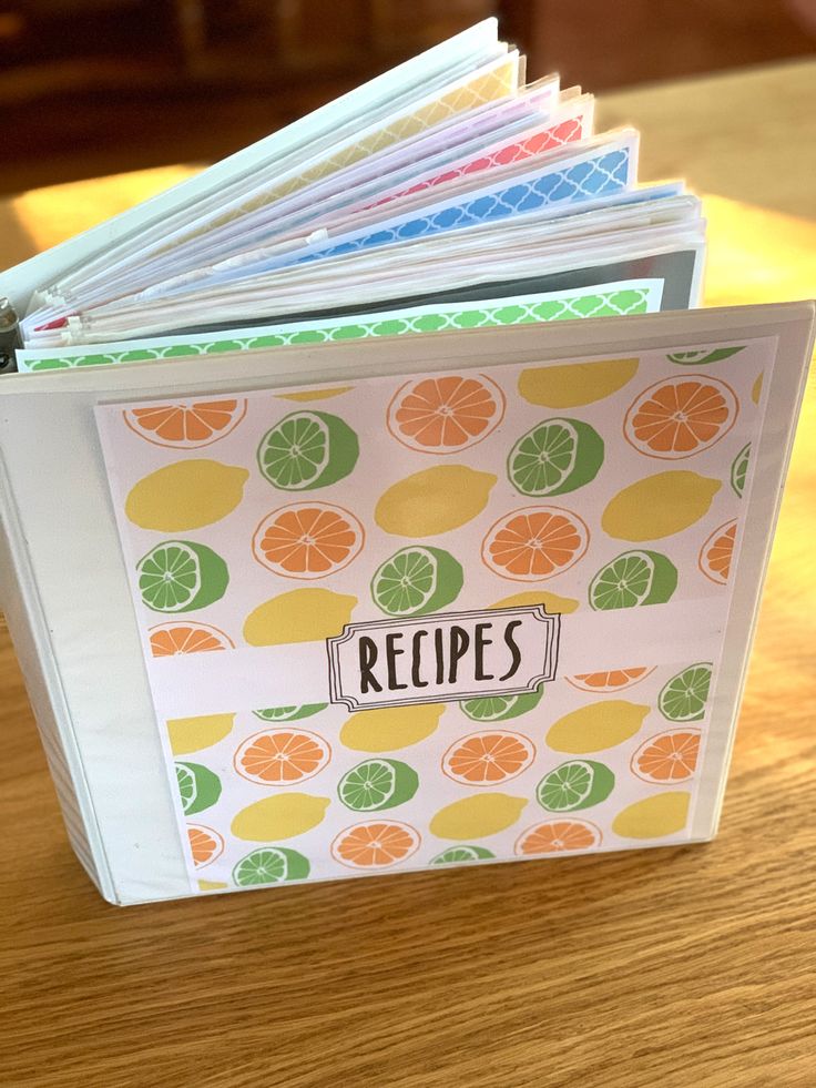 an open recipe book sitting on top of a wooden table filled with oranges and limes