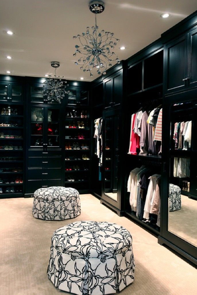 a walk in closet filled with lots of clothes and foot stools next to a chandelier