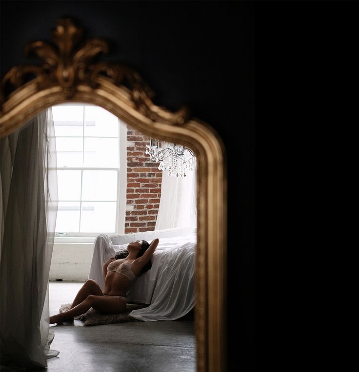 a naked woman laying on top of a bed in front of a golden framed mirror