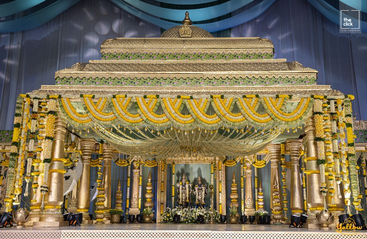 an elaborately decorated stage with gold columns and yellow flowers in the center is surrounded by blue drapes