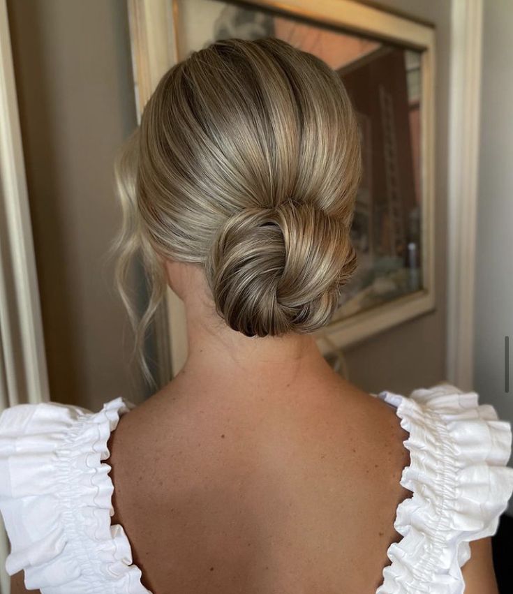 a woman with blonde hair wearing a white top and braid in her hair, looking at herself in the mirror