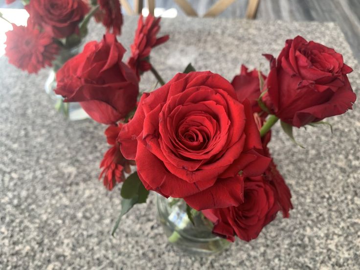 red roses are in a clear vase on the counter top, with one flower still blooming