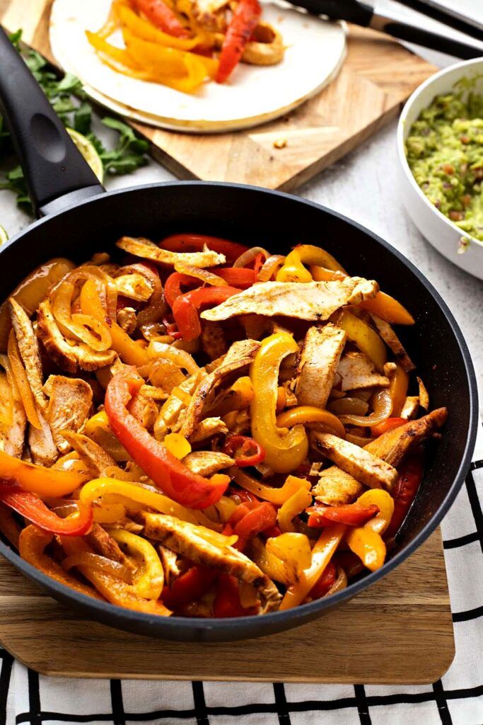 a pan filled with chicken and peppers on top of a wooden cutting board next to other food