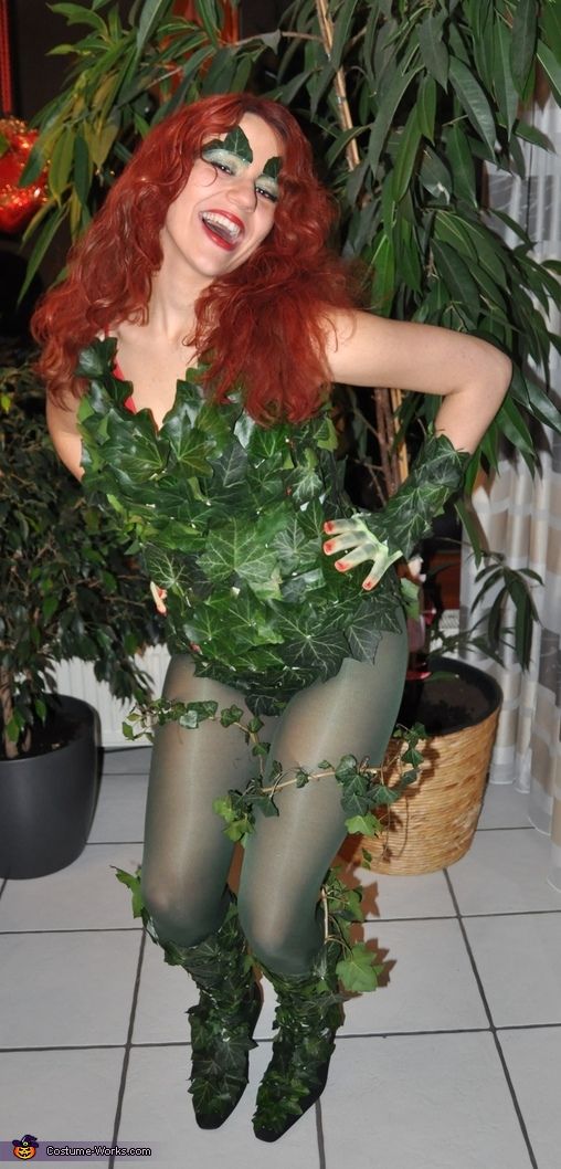 a woman with red hair and green makeup is sitting on the floor next to a potted plant