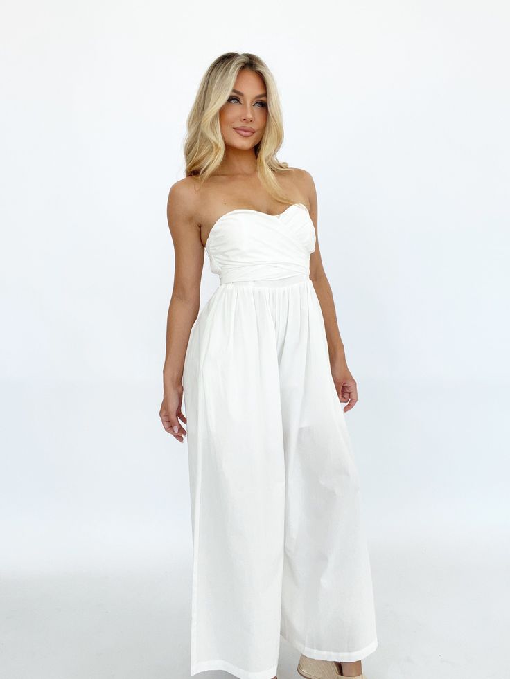 Effortlessly elegant, this versatile jumpsuit is perfect for any summer occasion. The bright and coastal design, featuring a lined and wide leg silhouette, makes it the perfect choice for a wedding, vacation, or resort getaway. The tie detail and strapless design exude luxury and style, while the stretchy smocked back panel ensures both comfort and a flattering fit. With pocket details for added convenience, this jumpsuit is a must-have for your summer wardrobe. Self 100% Cotton Lining 100% Poly Wide Leg Jumpsuit For Beach, Spring Strapless Wide Leg Jumpsuit, Wide Leg Jumpsuits For Beach In Spring, Wide-leg Jumpsuits And Rompers For Spring Beach, Wide Leg Jumpsuits And Rompers For Spring Beach, Elegant Beach Jumpsuits And Rompers, Chic Maxi Dress For Beach Wedding, Spring Beach Maxi Dress With Wide Leg, Summer Maxi Length Jumpsuits And Rompers