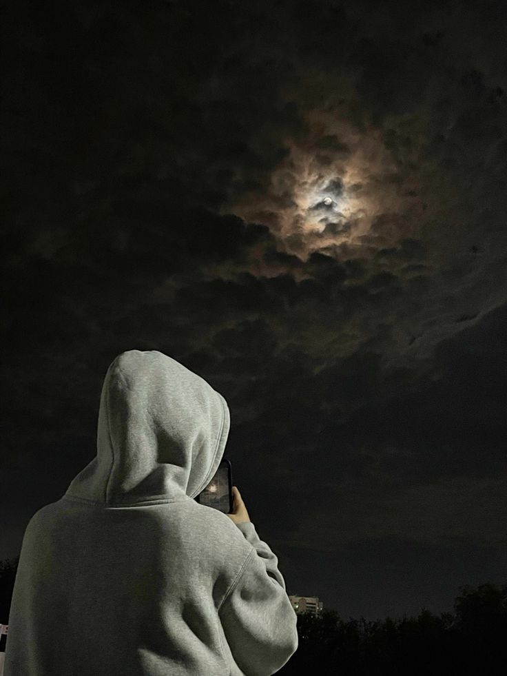 a person wearing a hoodie is looking at the moon