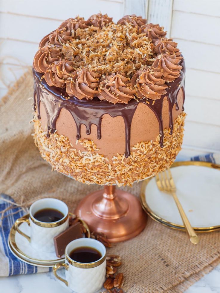 a cake with chocolate frosting and nuts on top sitting next to two cups of coffee