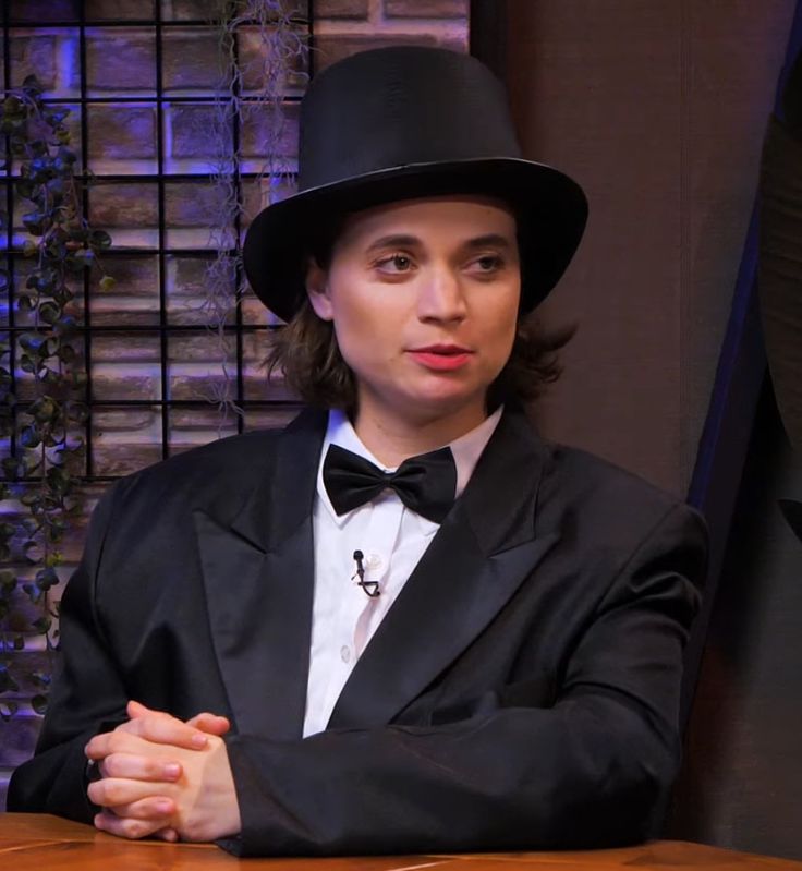 a man in a tuxedo sitting at a table with his hands folded up