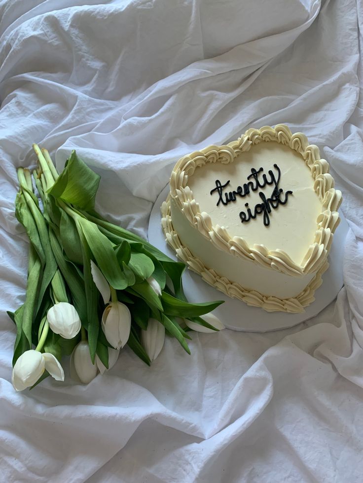 there is a cake and some flowers on the bed with white sheets in the background