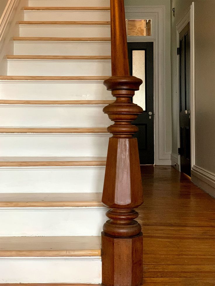 a cat sitting on top of a wooden banister next to a white wall and stairs