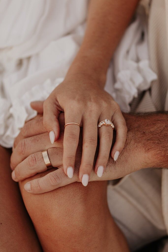 a man and woman holding hands with wedding rings on their fingers while sitting next to each other