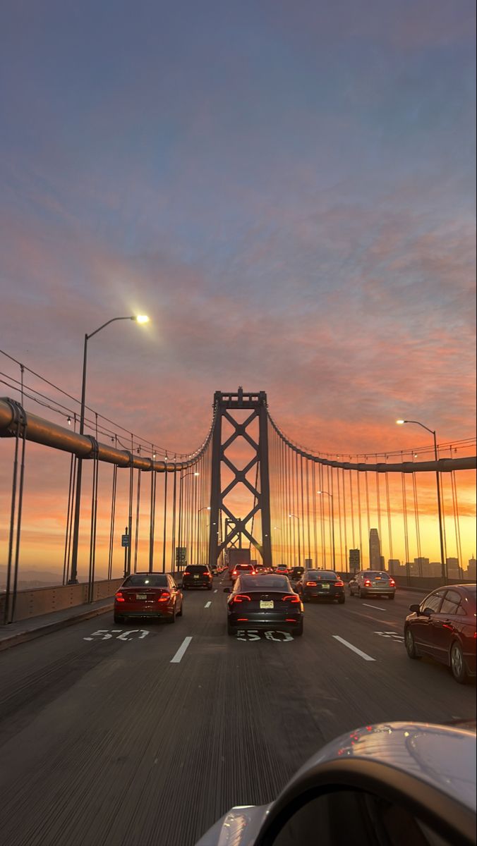 cars are driving over the golden gate bridge at sunset