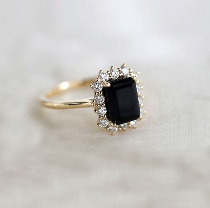 an engagement ring with a black stone surrounded by small white diamonds on a white cloth