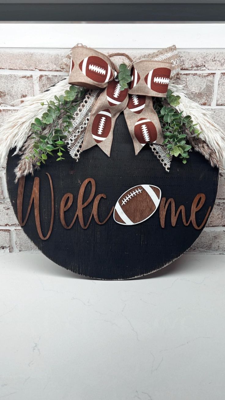 a welcome sign with footballs and greenery on the top, in front of a brick wall