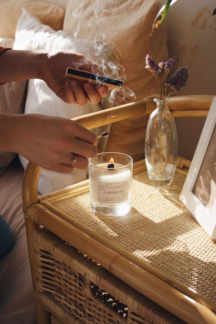 a person is lighting a candle on a wicker table next to a glass vase