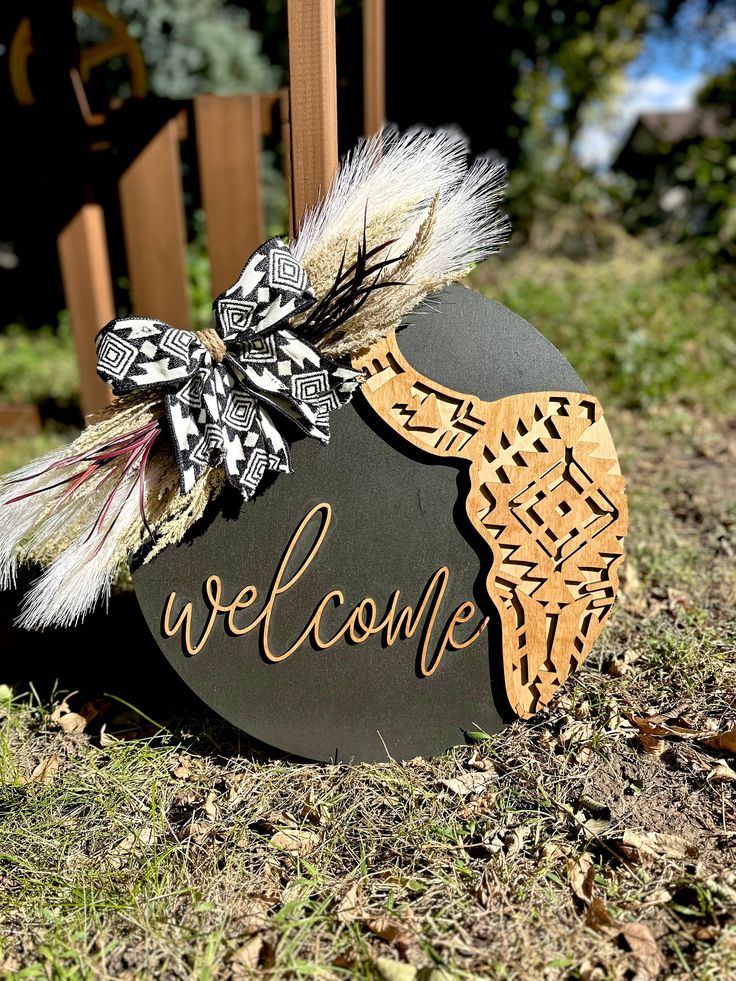 a welcome sign with feathers on it sitting in the grass next to a wooden fence