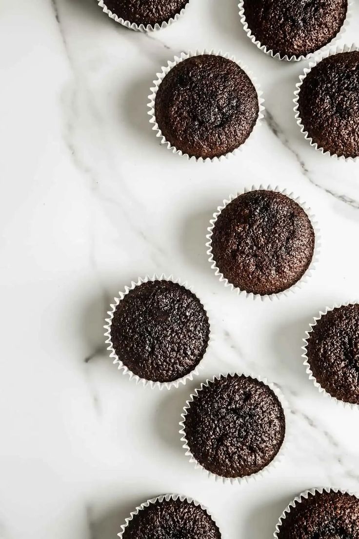 twelve chocolate cupcakes lined up on a marble surface